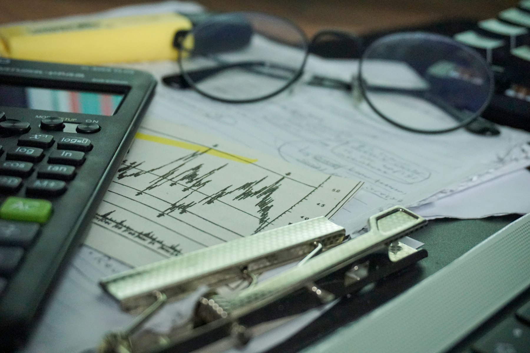 A calculator, reading glasses and working papers on a desk
